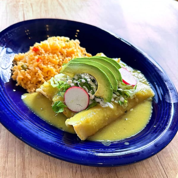 Mexican enchiladas with green sauce, avocado, radish, and rice on a blue plate.