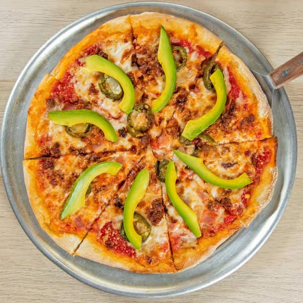 Mexican pizza with chorizo, jalapeños, and avocado slices on a metal tray.