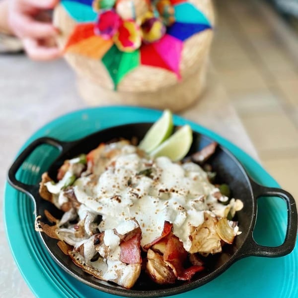 A cast iron skillet of La Ingrata's Mexican food, topped with cream, bacon, and lime wedges.