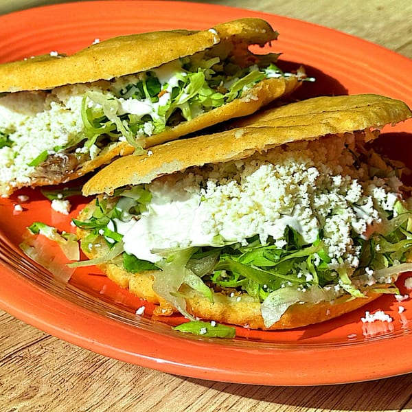 Two La Ingrata sopes, filled with meat, lettuce, sour cream, and crumbled cheese on an orange plate.
