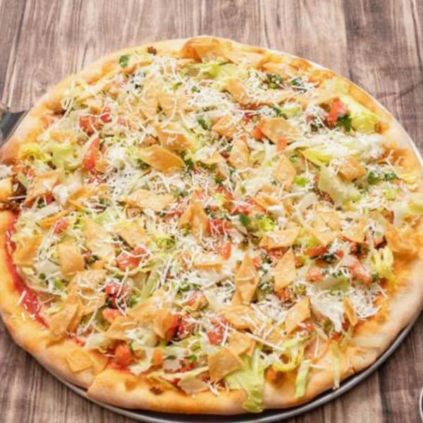 A large Mexican pizza with lettuce, tomatoes, cheese, and tortilla chips on a wooden table.