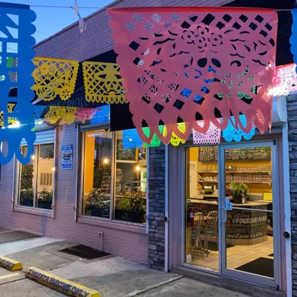 Exterior of La Ingrata Camden, a Mexican restaurant, adorned with colorful papel picado banners at dusk.
