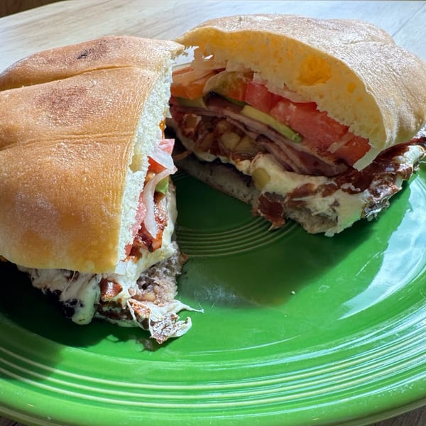 A Mexican torta, sliced in half, revealing layers of meat, cheese, avocado, tomato, and onion on a green plate.